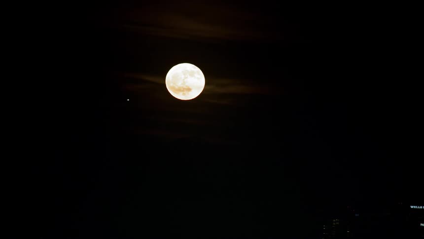 A city skyline at night with the moon in the background