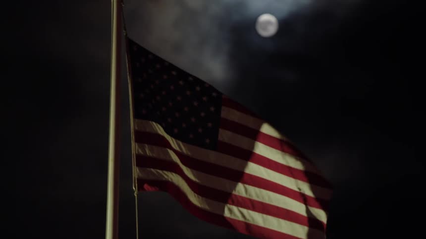 An american flag waves in the wind on a cloudy night