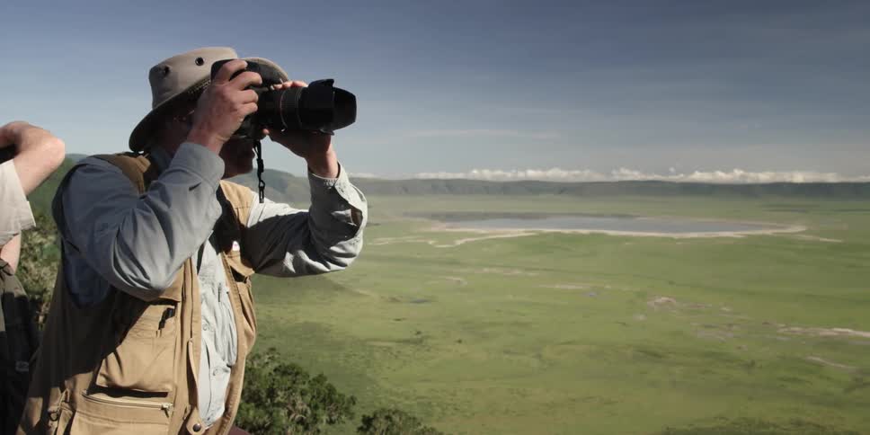 A man is standing on a hill taking photographs on a sunny day