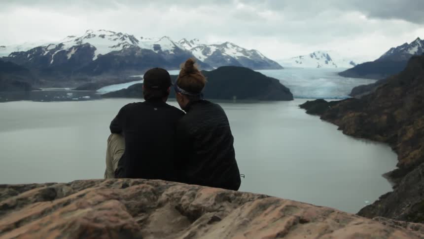 A man and woman kiss as they sit above a lake