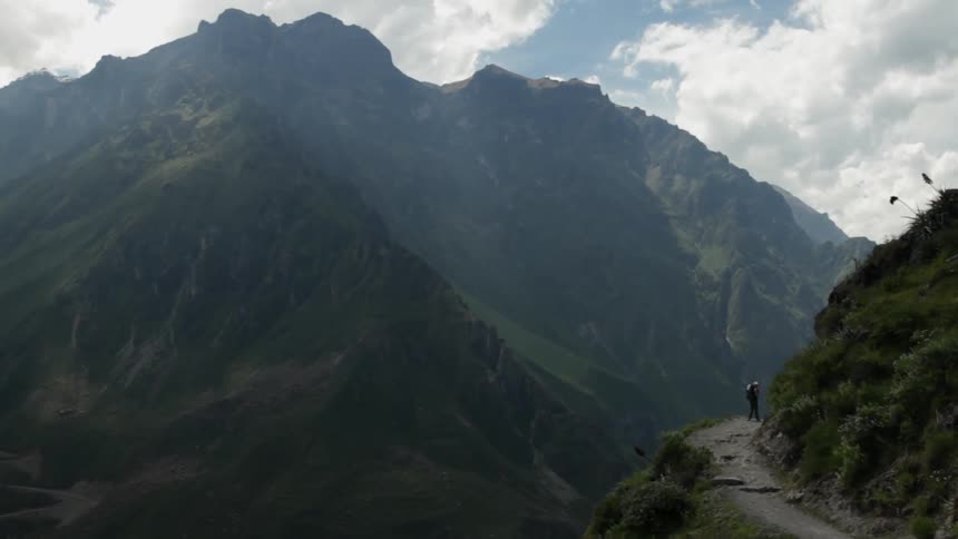 A man stands on a mountain trail on a cloudy day