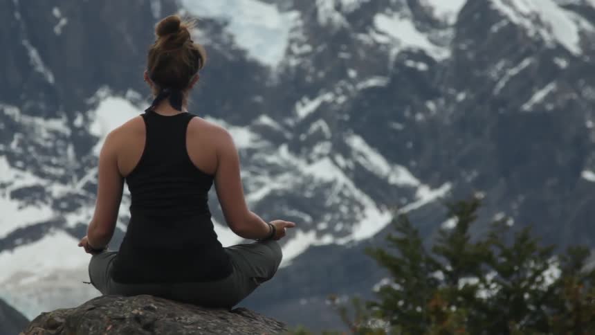 A woman in a black shirt meditates on a mountain