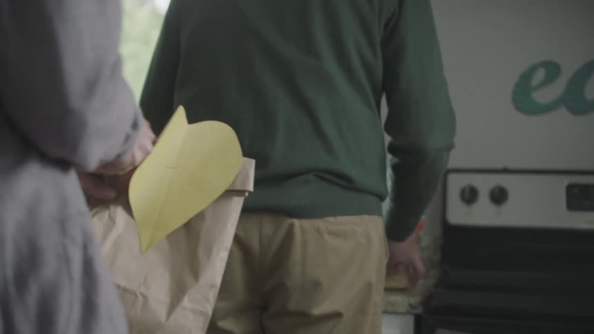 Two people carry things inside to their home kitchen and place them on the counter