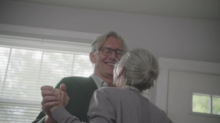 An elderly couple dances on wood floor in their home
