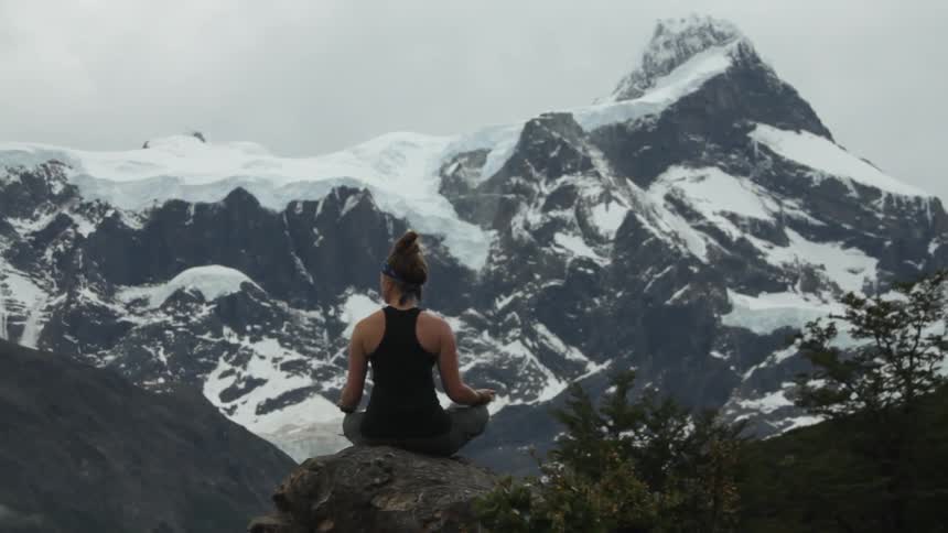 A woman is sitting on the top of a rock looking at a snow covered mountain
