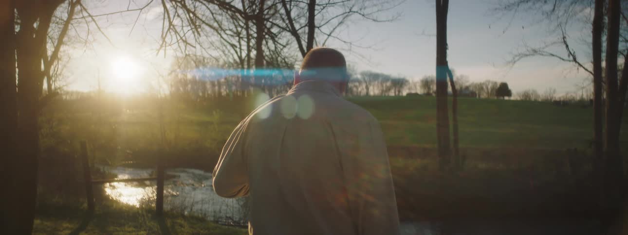 A man stands watching the sunlight shimmer on the surface of a stream