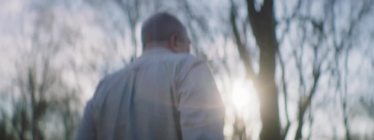 A man walks out of a garage towards a river while carrying a gun