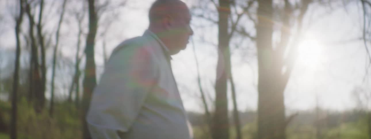 An elderly man walking through a woodland while looking around fearfully