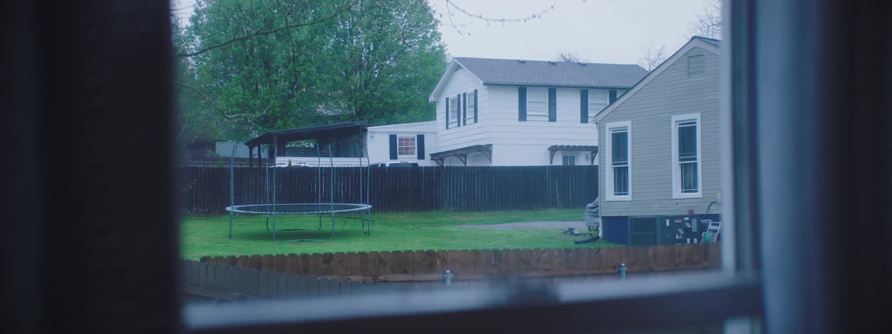 The trampoline in the empty yard next door on a rainy day is visible through the window