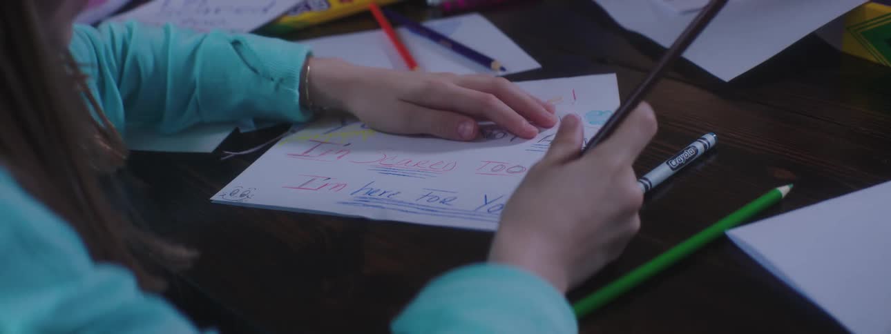 Girl sitting at table writes on paper using colored pencil