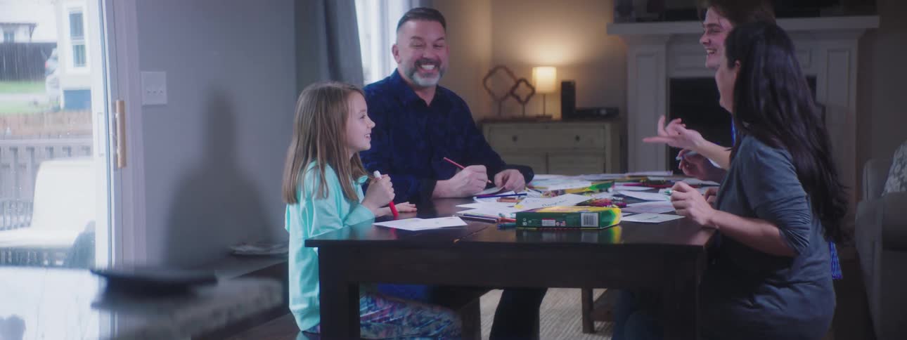 A family sits at a table laughing and drawing