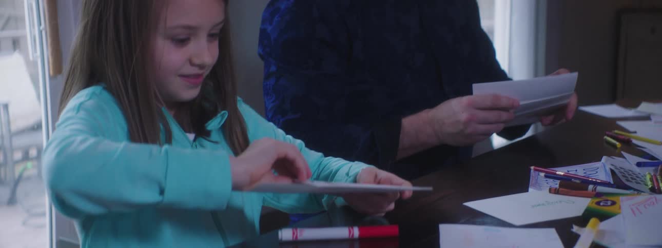 A girl stuffs a card she made into an envelope while she and her family make cards with crayons and markers