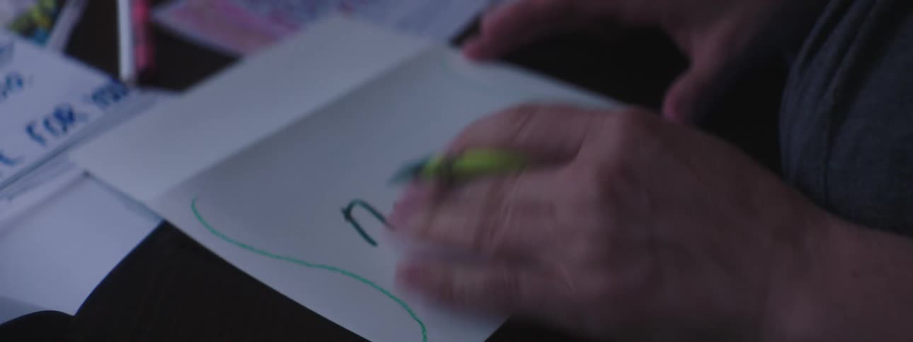Woman sitting at table writes with crayon on paper