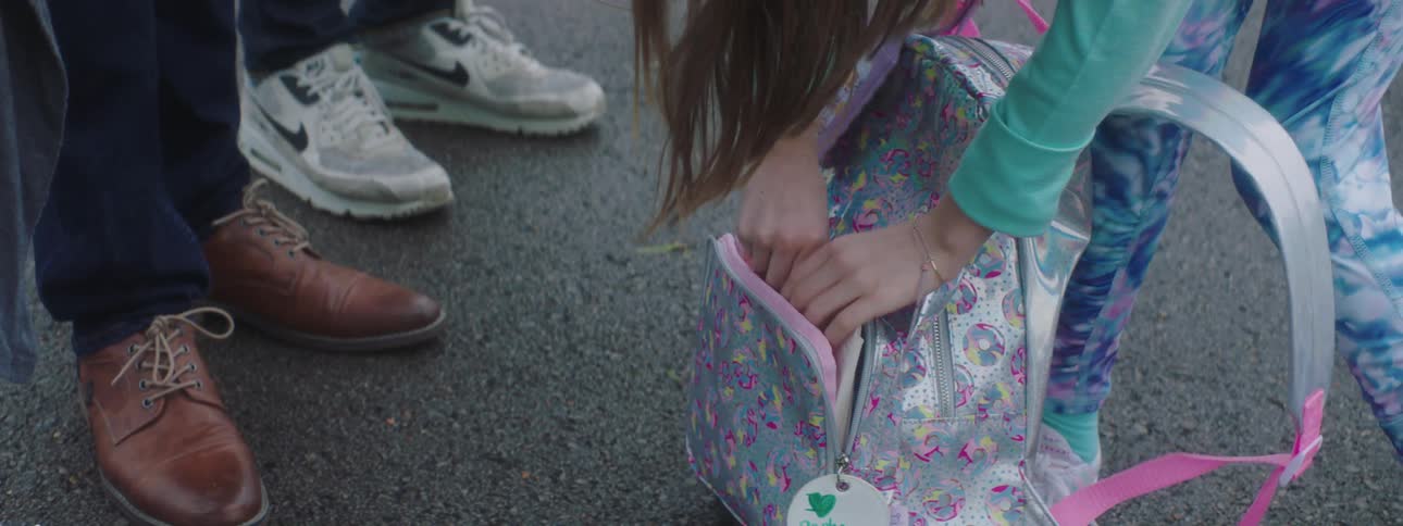 A girl unzips her school backpack and removes several cards while her family stands near her