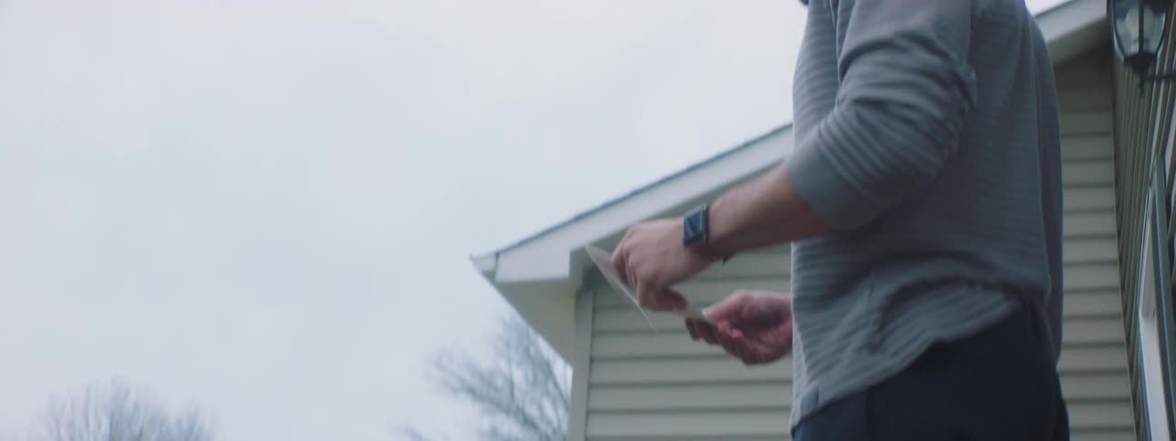 Man picks up note from door mat and looks around his neighborhood