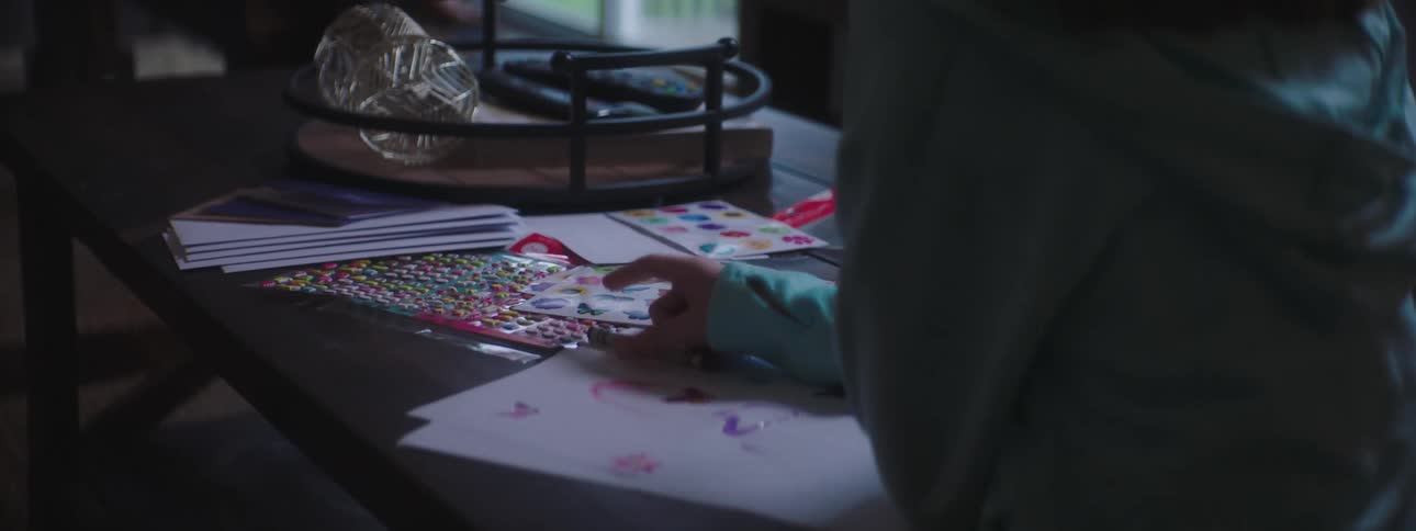 A girl sits at a table and colors with crayons and stickers