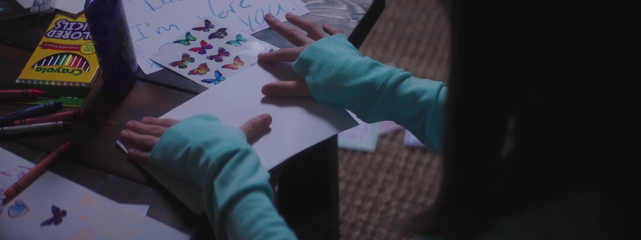 A girl makes an envelope and uses a crayon to write on the front of it