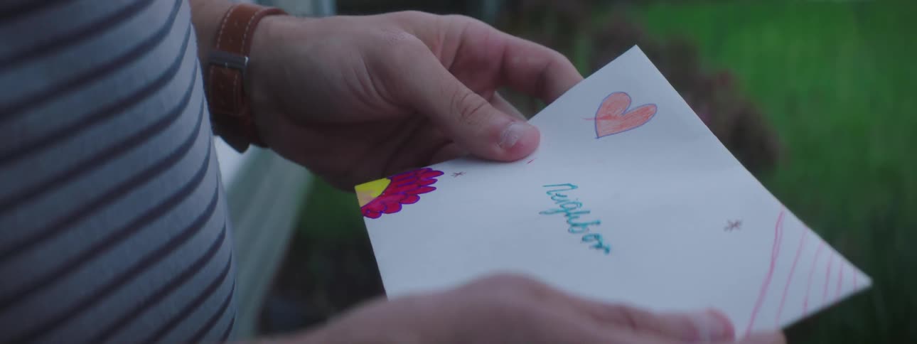 A man bends over to pick up a childs drawing found at the front door of his home