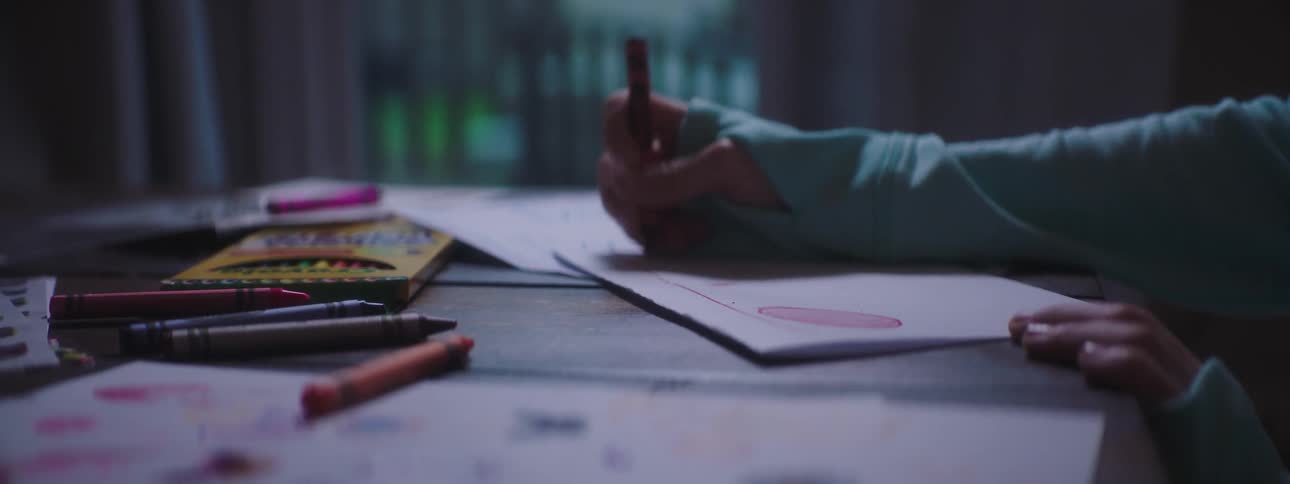 Kid drawing with crayons on paper over table