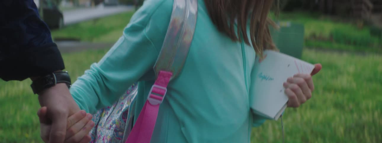 A little girl holds her dads hand and carries letters