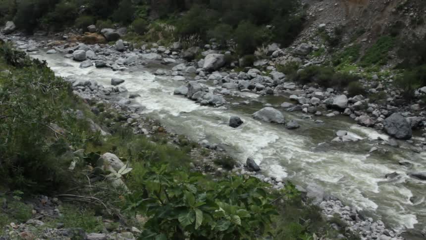 A small stream is moving fast past two hillsides