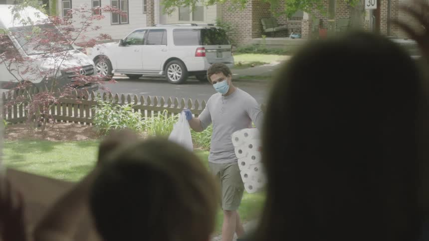 Man delivering groceries returns greeting of children inside house