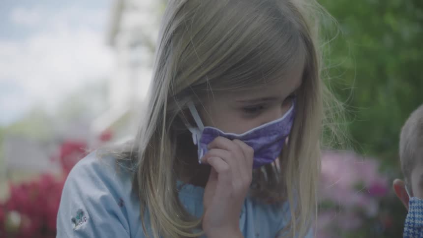 A girl sitting outside in her yard takes off her protective mask so she can use her inhaler