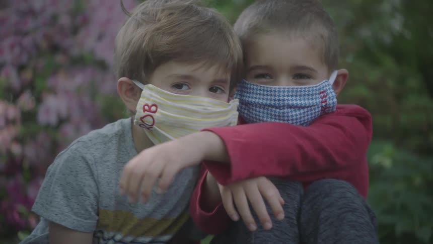 Kids wearing face masks hug and fall on lawn