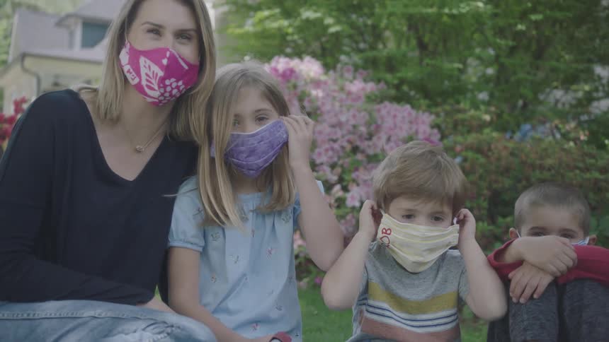 Mother and children wearing face masks sit on the grass in the garden