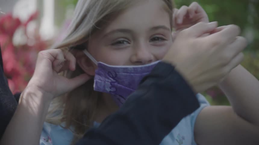 Mother helps daughter wear a face mask in the garden