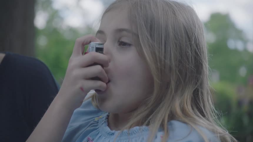 A little girls uses an inhaler as her mom watches