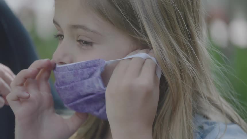A woman helps her daughter put a mask on her face
