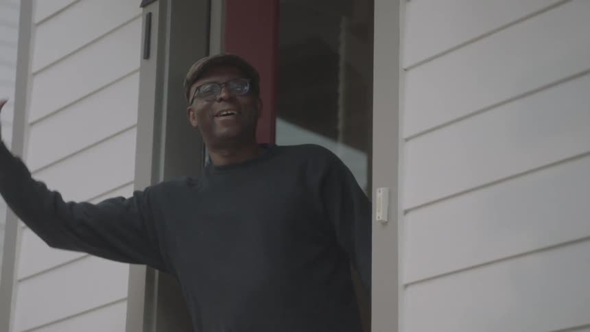 A woman walks away from a front door where a man opens it and picks up a box of groceries front his front step