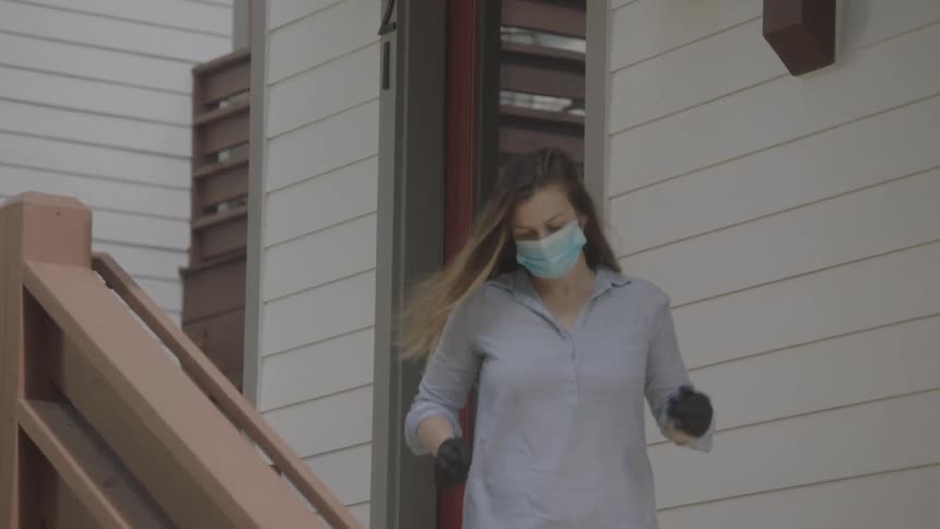 A woman wearing a mask and gloves delivers a box of items to the porch of a man