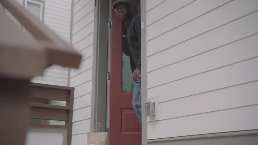 Woman leaves food bags on the doorstep and knocks the door then moves away just to wave at the black man during the pandemic due to the coronavirus