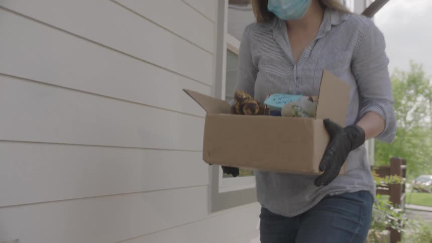 Woman wearing face mask and gloves delivers box to apartment porch then leaves