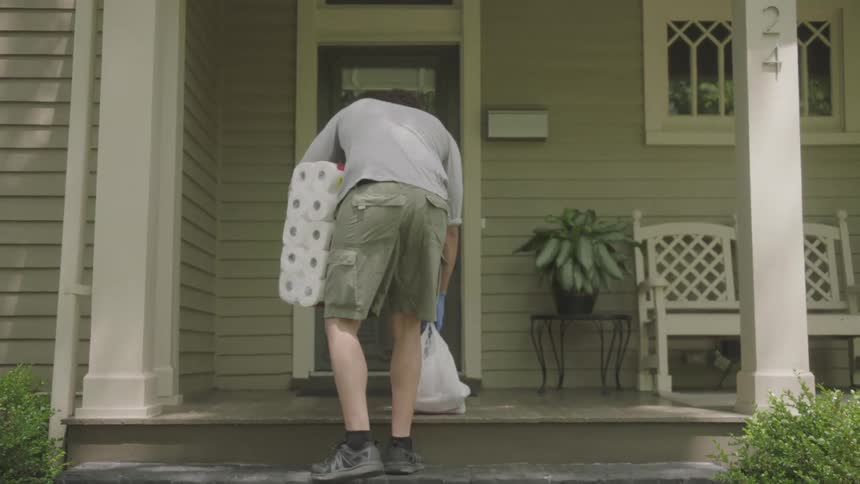 Man wearing surgical mask and gloves delivers groceries to a home