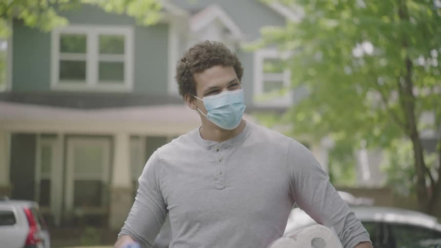 Man wearing face mask and gloves carries groceries