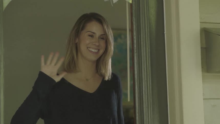 A woman looks through a window and waves