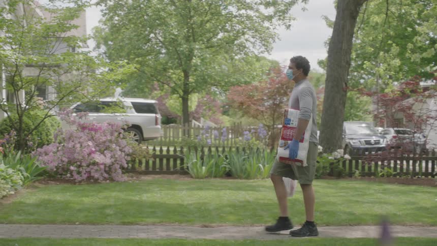 Man walks through yard onto porch carrying groceries