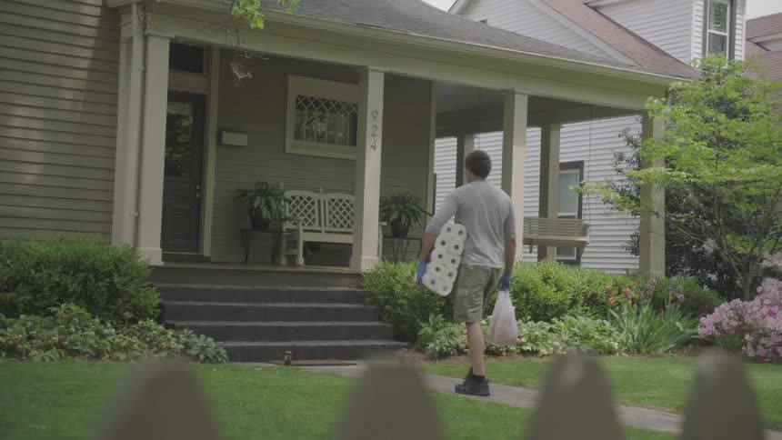 A man carries paper products up to a house