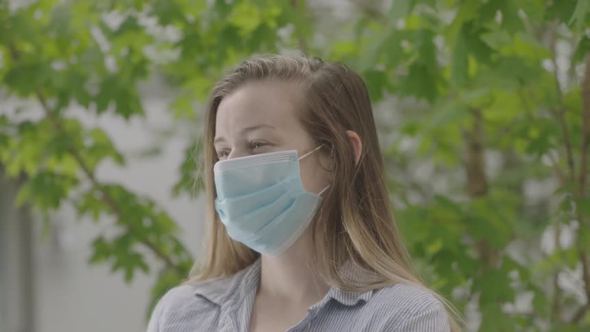 Woman wearing a surgical mask and gloves holds a box of groceries