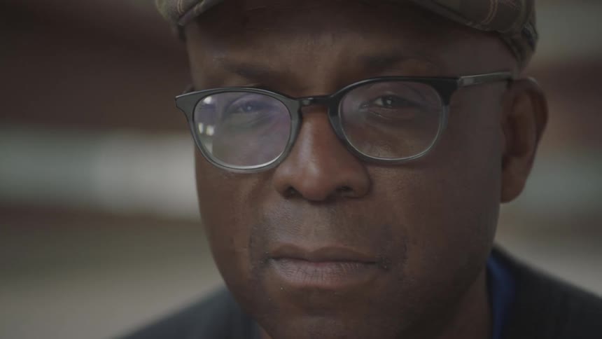 Black man has a faraway look in his eyes and turns his head to the camera smiling