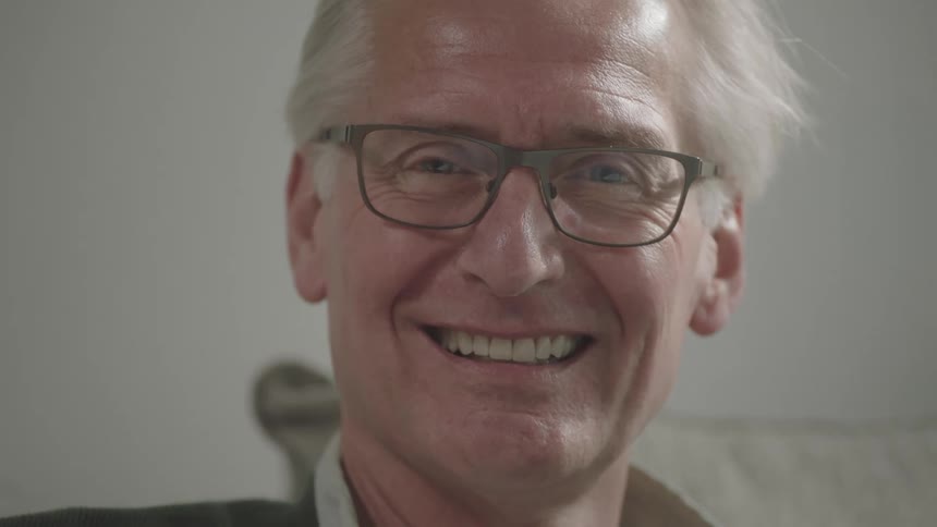 Elderly man sitting on the sofa smiles broadly in the living room at home