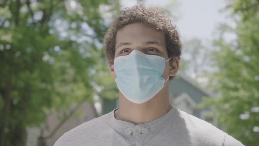 Man wearing mask stands outdoors in neighborhood at day