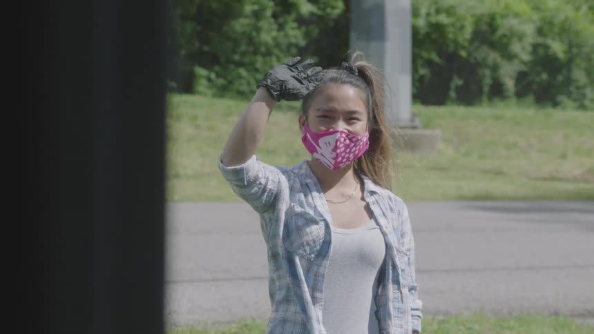 Woman wearing a surgical mask and gloves waves then turns and walks away