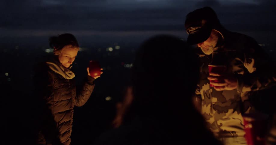 A group of people drinking and dancing around a fire at night