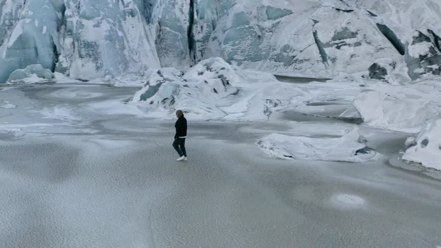 Man walks across the icy lake surrounded by glaciers