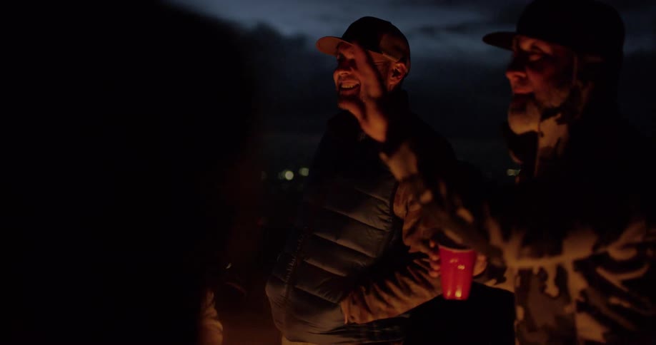 A group of men stand around a campfire at night