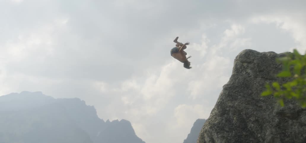 A man jumping off a cliff and doing a back flip before diving into the lake below
